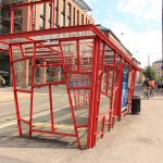 Ein Buswartehäuschen aus roten Metallstreben und Glas