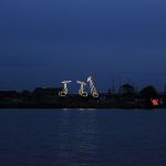 Lichtinstallation, bei der die Konturen von drei Hafenkränen beleuchtet werden